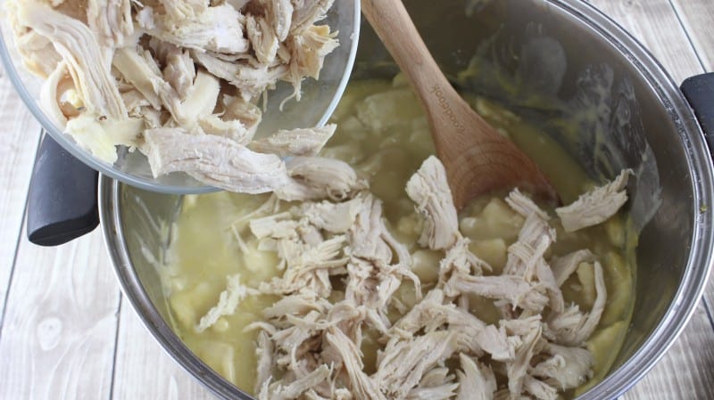 Pouring shredded chicken into pot with dumplings.