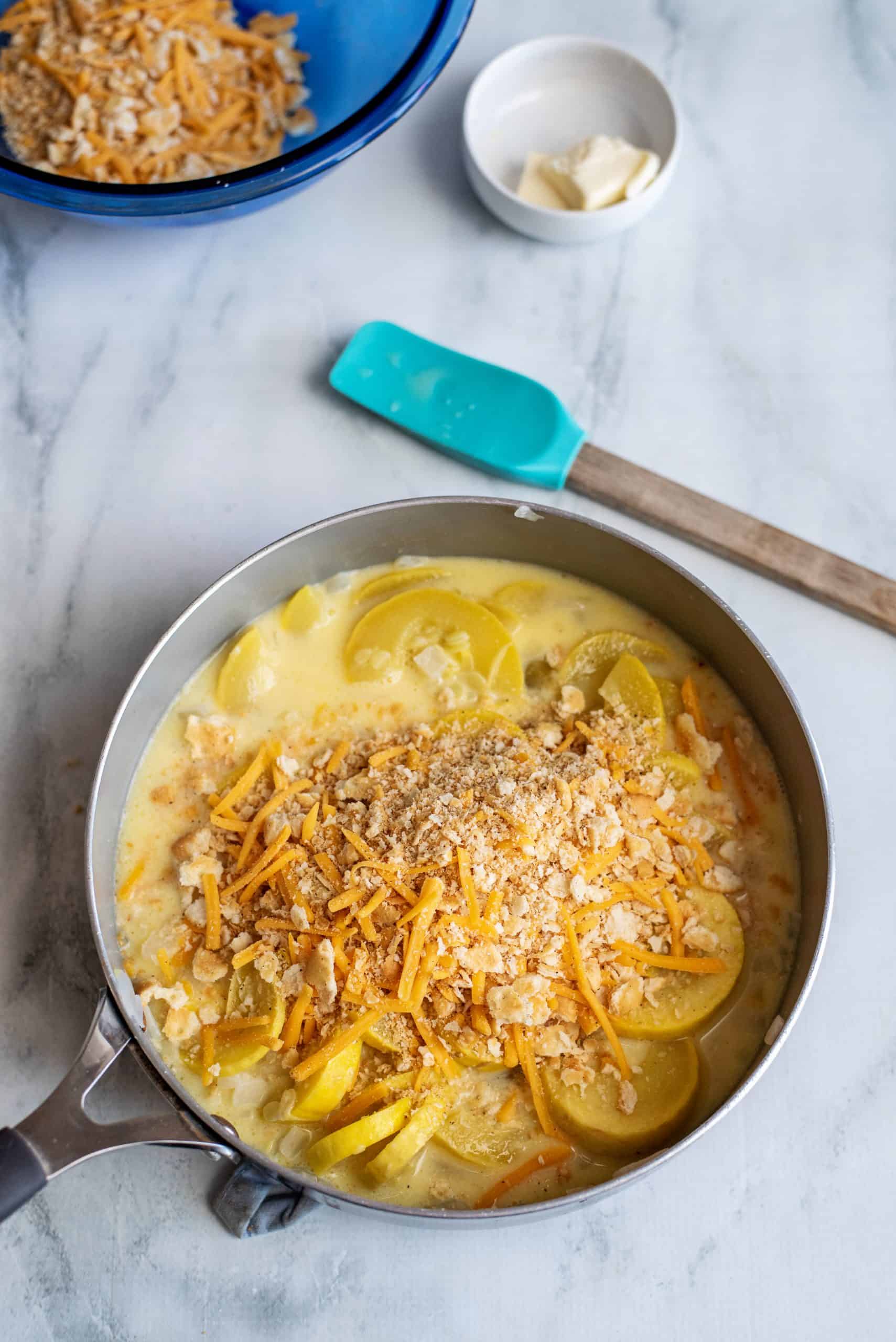 Cracker and shredded cheese piled on sliced squash in a skillet.