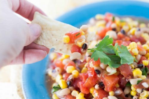 Scooping Texas caviar out of bowl with corn chip.