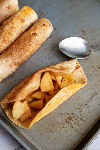 Spooning spiced apple filling onto a flour tortilla before rolling.