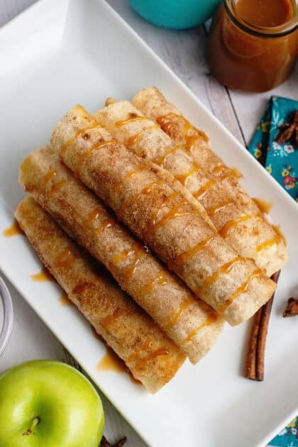Hero shot: Six golden apple flautas arranged on a white serving platter with drizzles.