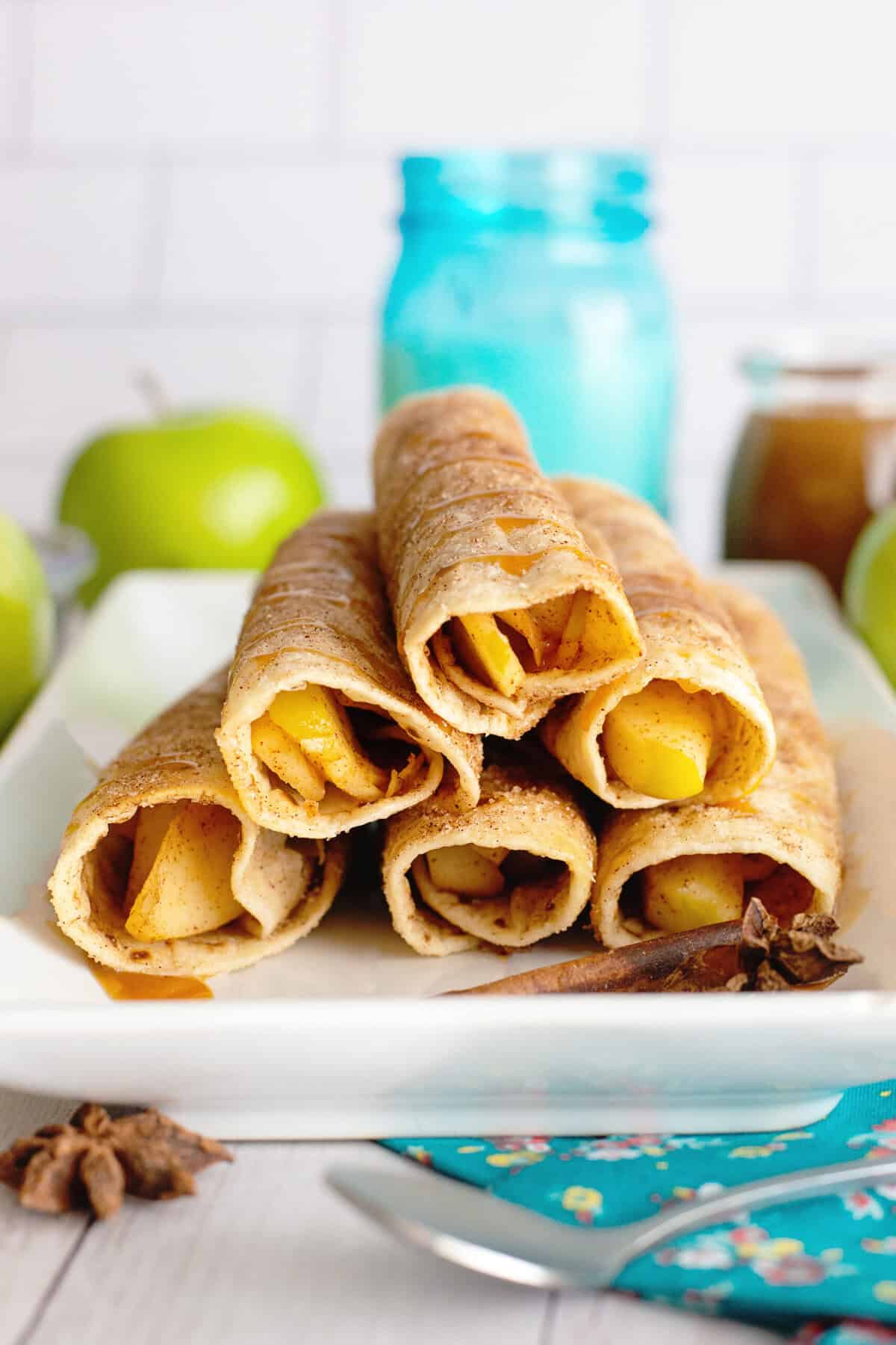 Six golden apple flautas arranged on a white serving platter with drizzles.