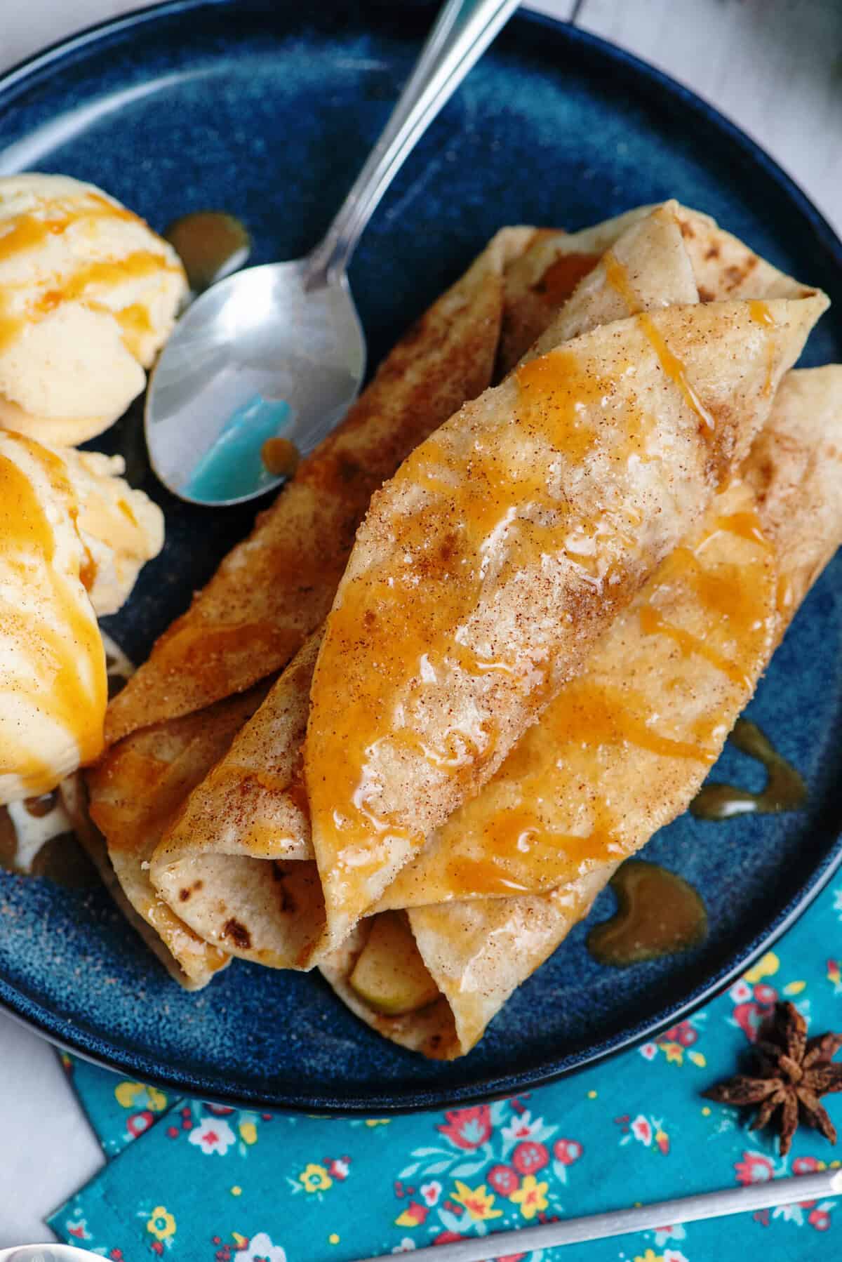 Apple flautas with powdered sugar and cinnamon glaze on a blue ceramic dish.