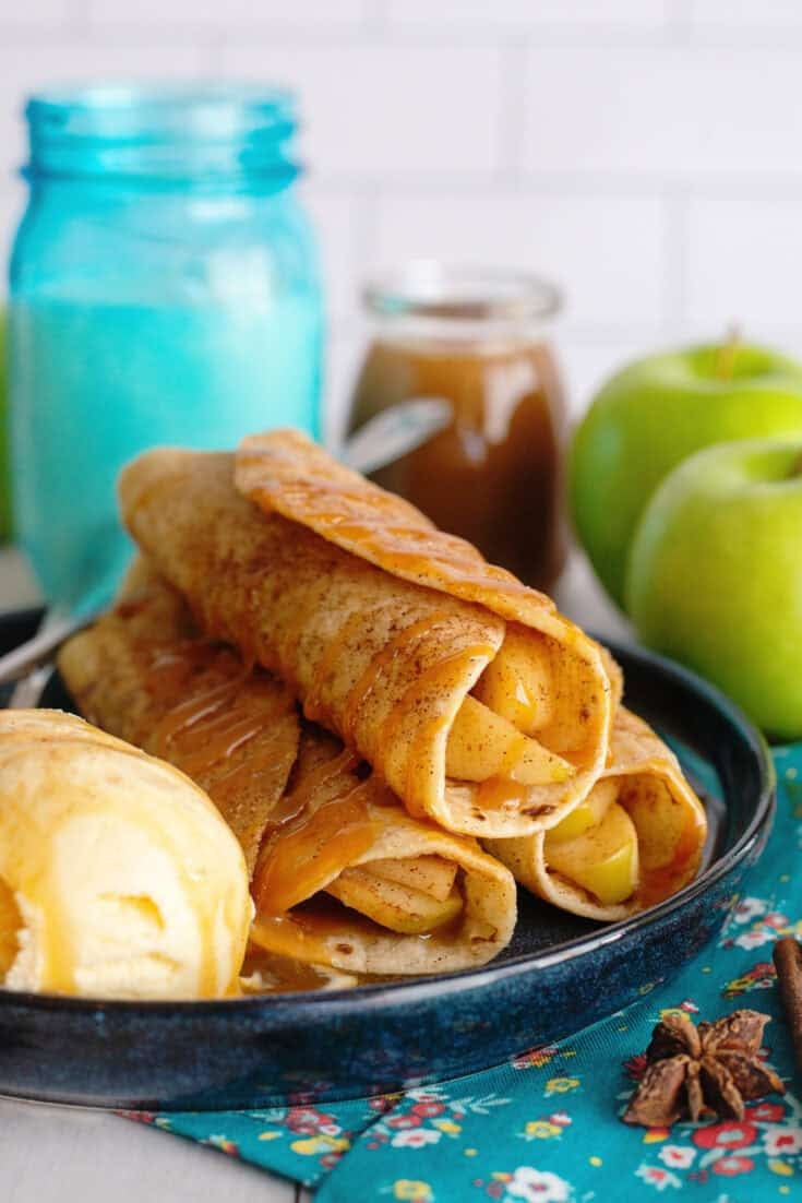 Four crispy apple flautas drizzled with caramel sauce on a blue plate.