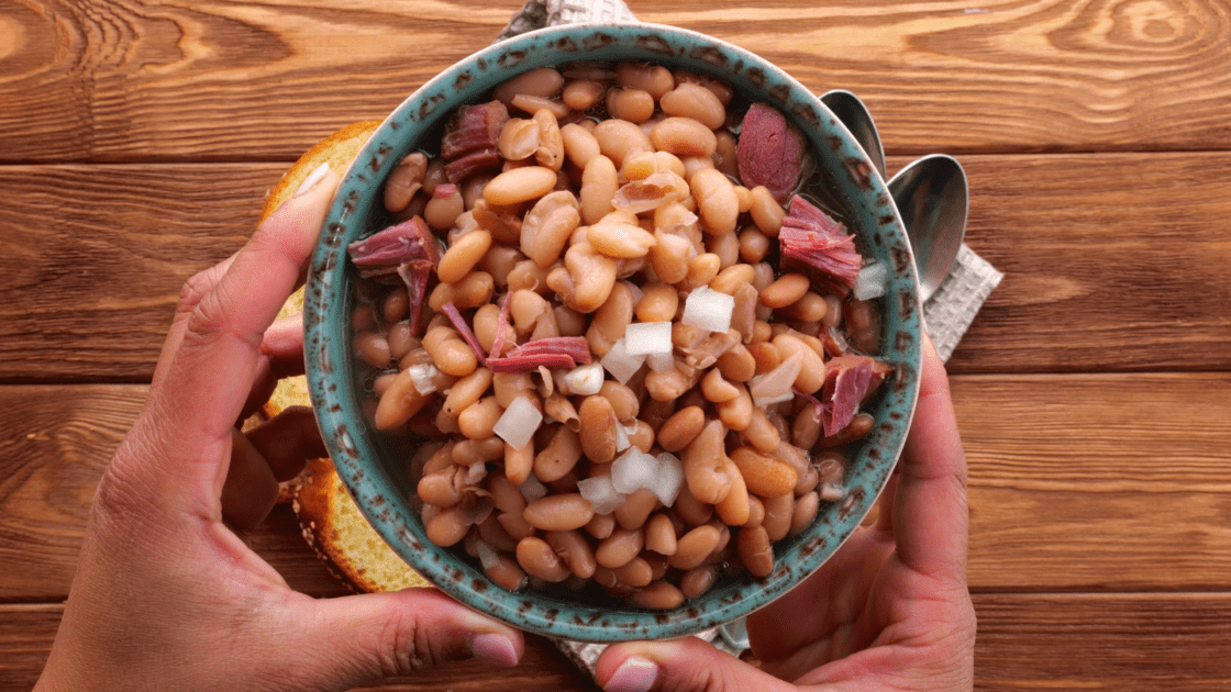 Hands holding a bowl of pinto beans and ham.
