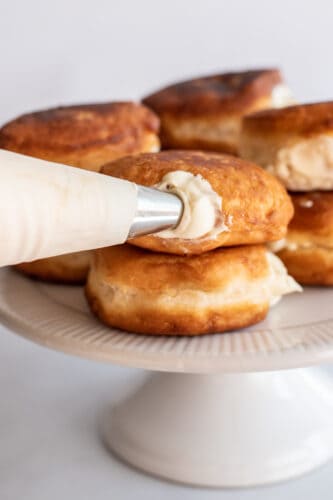 Piping filling into the mini Boston cream pies doughnuts.