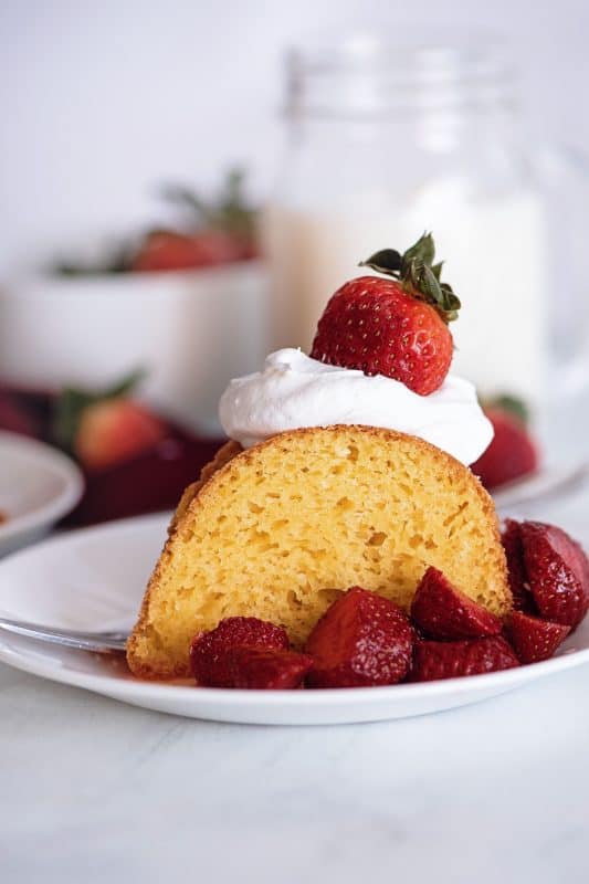 Slice of simple vanilla cake with whipped cream and strawberries.
