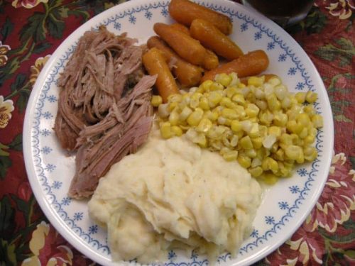 Plate of crock pot pork roast with carrots, corn, and mashed potatoes.