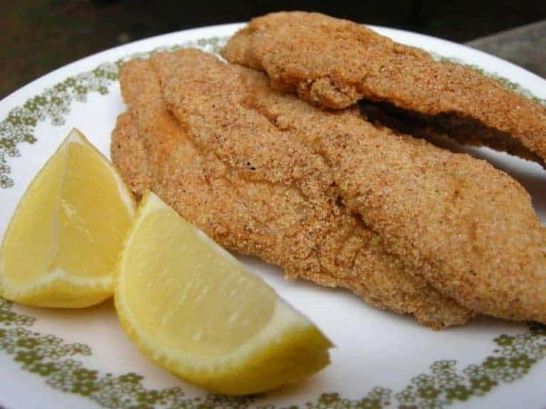 Fried catfish on plate with lemon wedges.