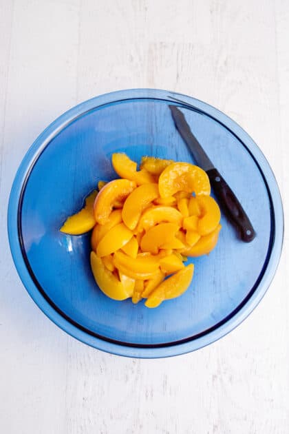 Sliced peaches in a glass blue mixing bowl.