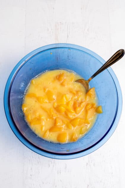 Wet ingredients for peach cobbler muffins in a glass blue mixing bowl.