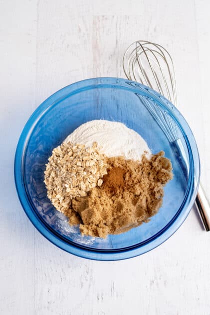 Oats, cinnamon, brown sugar, and flour in a glass blue mixing bowl.