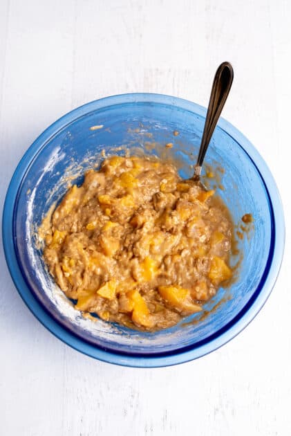Batter for peach cobbler muffins in a glass blue mixing bowl.