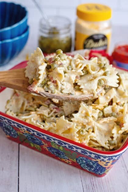 A serving dish of Velveeta bowtie pasta with a wooden spoon scooping some out.