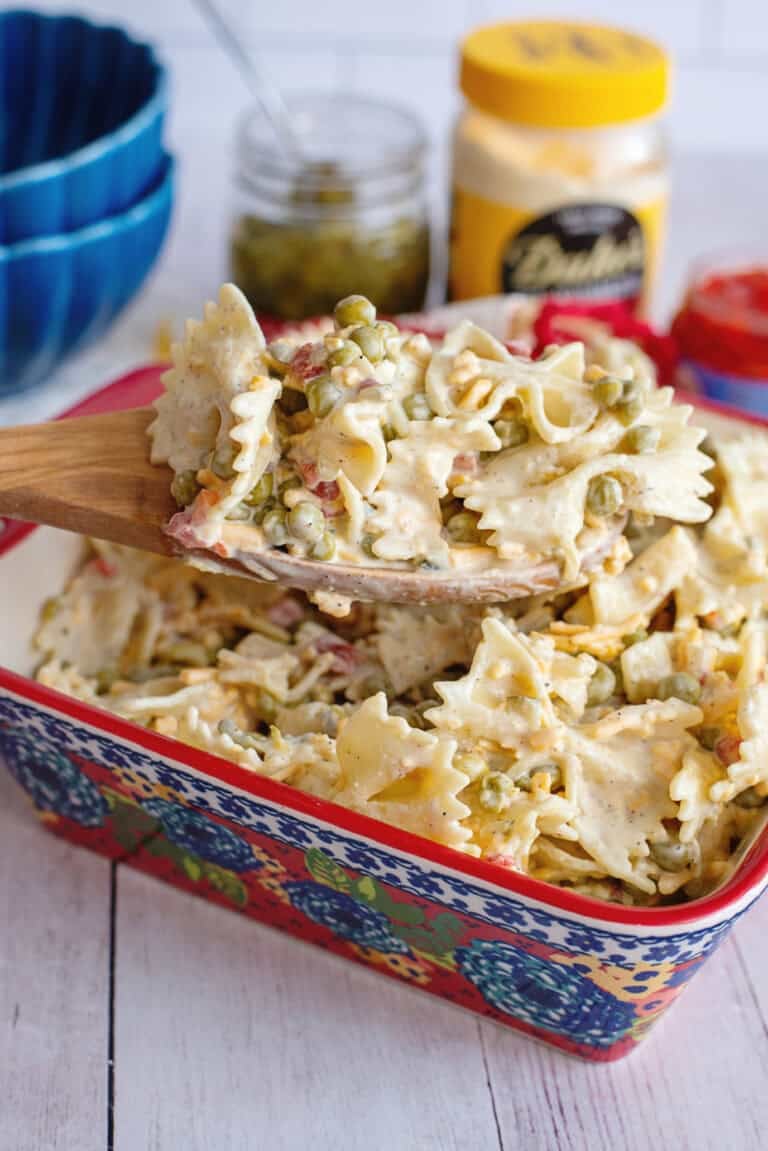 A serving dish of Velveeta bowtie pasta with a wooden spoon scooping some out.