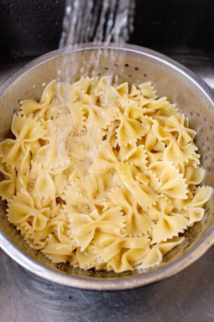 Rinsing cooked bowtie pasta with cold water.