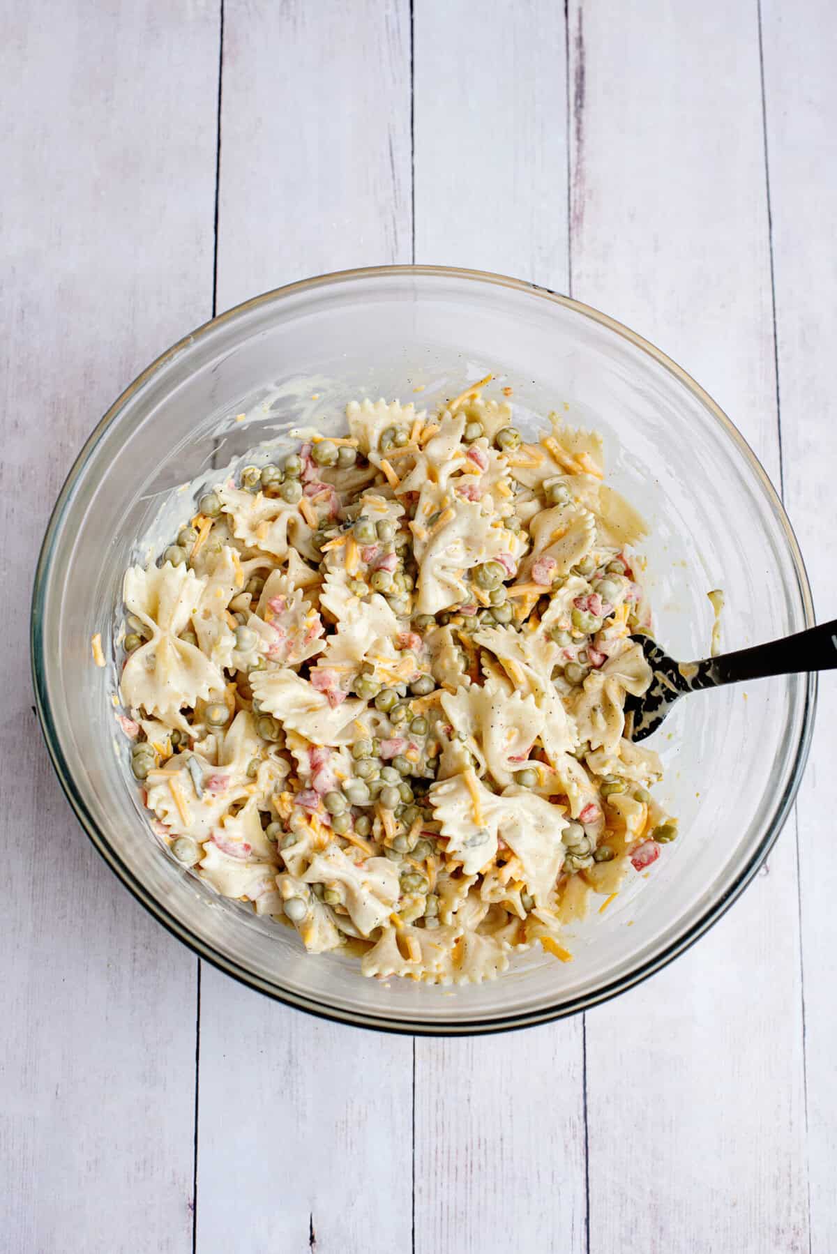 Mixing the bowtie pasta with the dressing in a glass bowl.