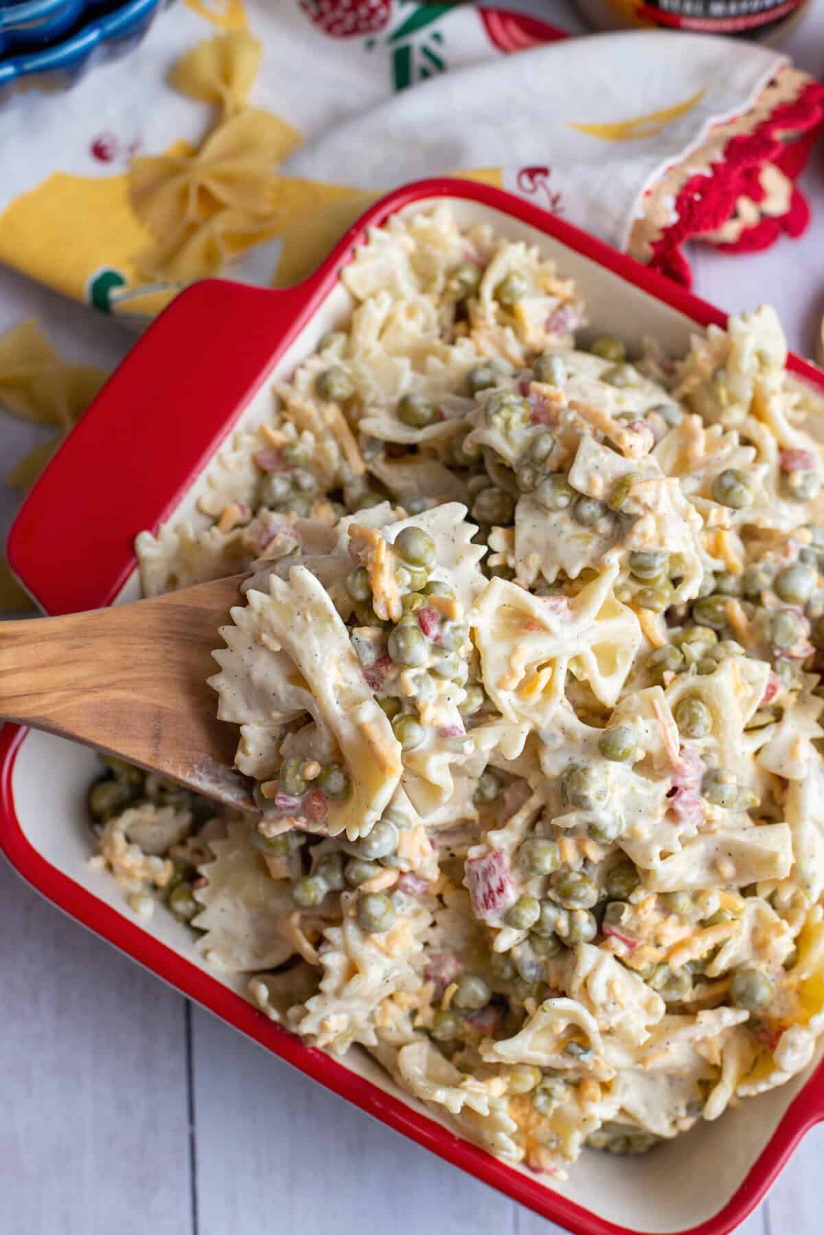 A serving dish of Velveeta bowtie pasta with a wooden spoon scooping some out.