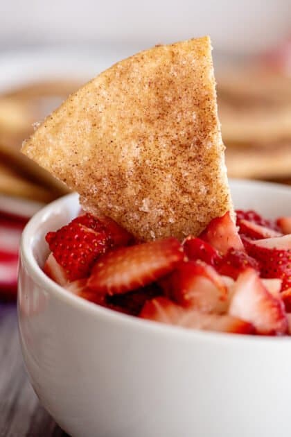 Cinnamon tortilla chip dipping into a bowl of strawberries.