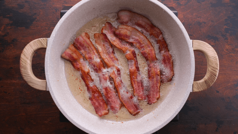 Bacon strips frying in skillet