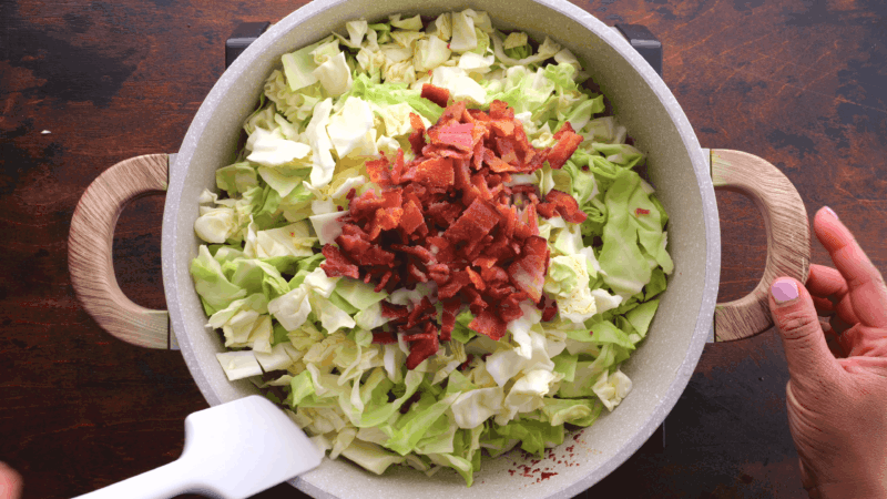 Crumpled fried bacon on top of cabbage in skillet.