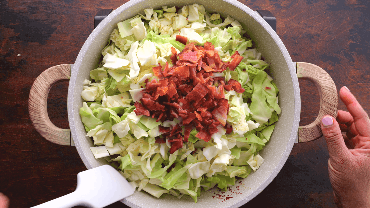 Crumpled fried bacon on top of cabbage in skillet.