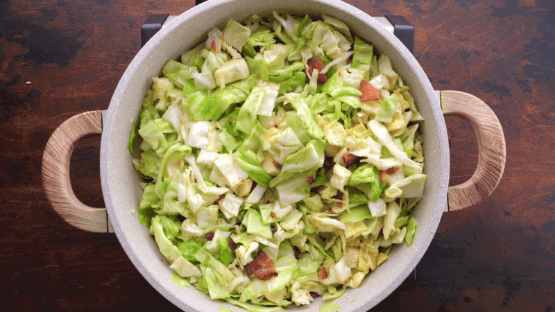 Tossed fried cabbage with bacon in skillet.