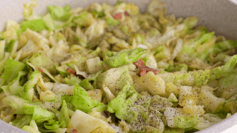 Salt and pepper covering fried cabbage with bacon.