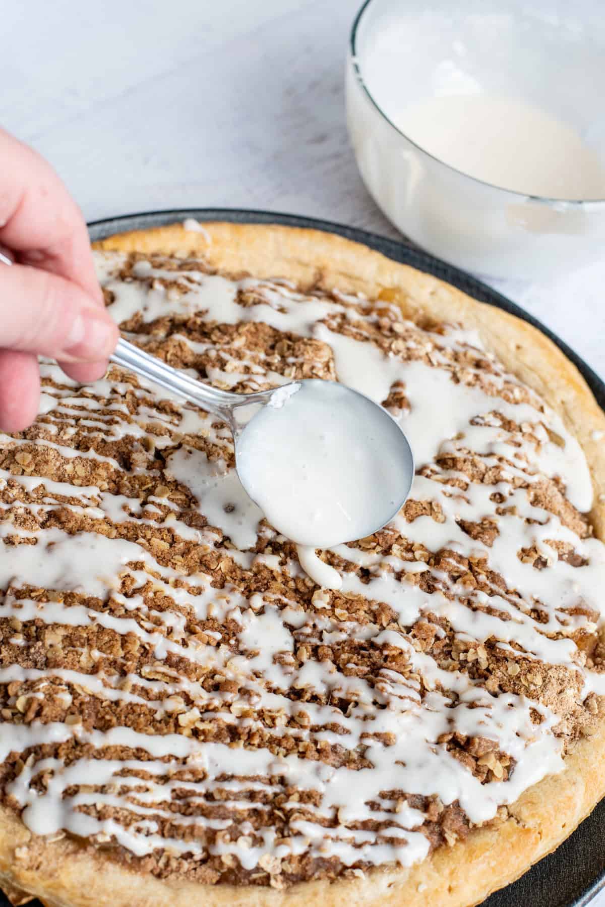 use a spoon to drizzle glaze on top of the baked apple pie pizza