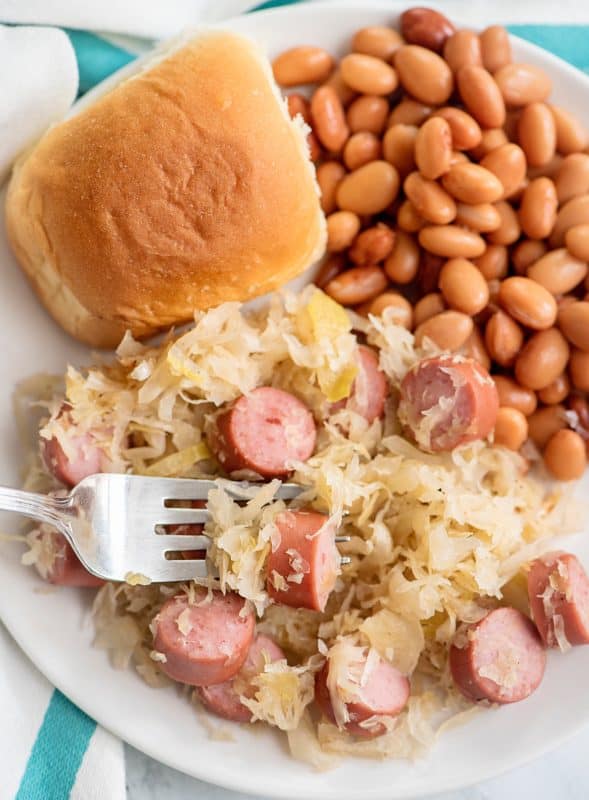 Sauerkraut and weenies on plate with beans and bread roll.