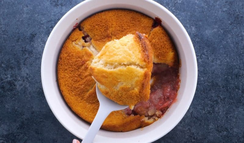 Removing slice of strawberry cobbler from baking dish.