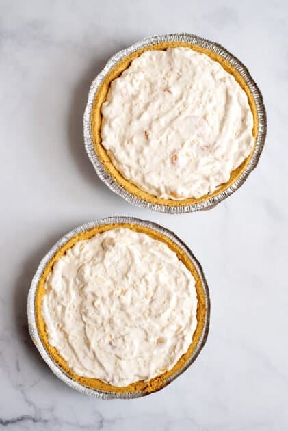 Spoon filling into two graham cracker crusts.