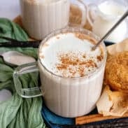 Vanilla chai tea on a blue plate with a spoon beside spices and baked goods.