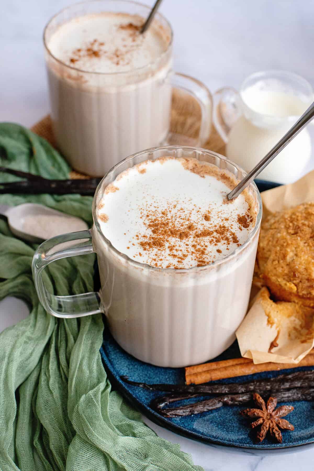 Vanilla chai tea on a blue plate with a spoon beside spices and baked goods.
