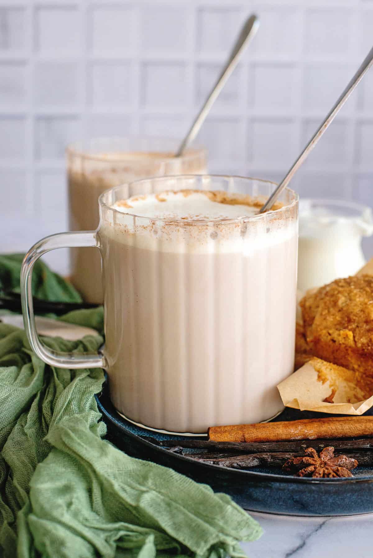 Vanilla chai on a blue plate with a spoon besides a baked good and spices.
