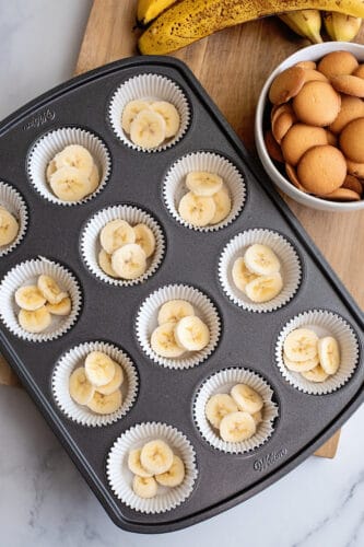 Adding banana slices to muffin papers in muffin tin.