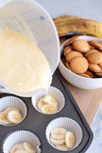 Pouring pudding mixture over banana layers in cups.