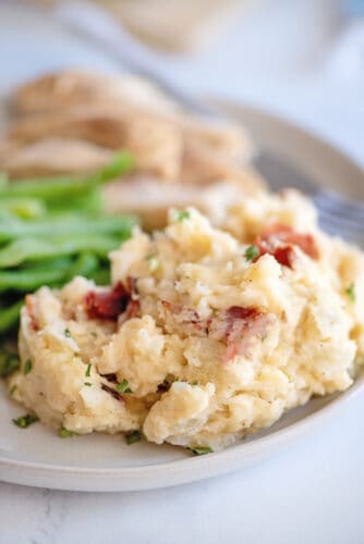 Mashed potatoes on plate with green beans and turkey in background.
