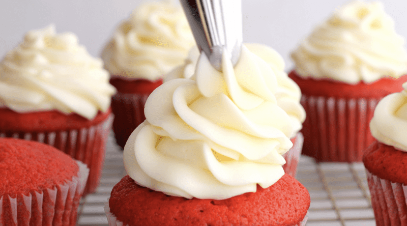 Piping cream cheese frosting onto your red velvet cupcakes.
