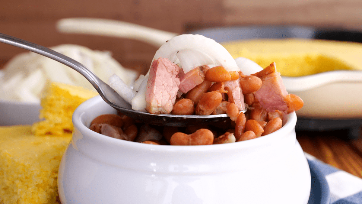 Spoonful of pinto beans and ham with pickled onions on top.