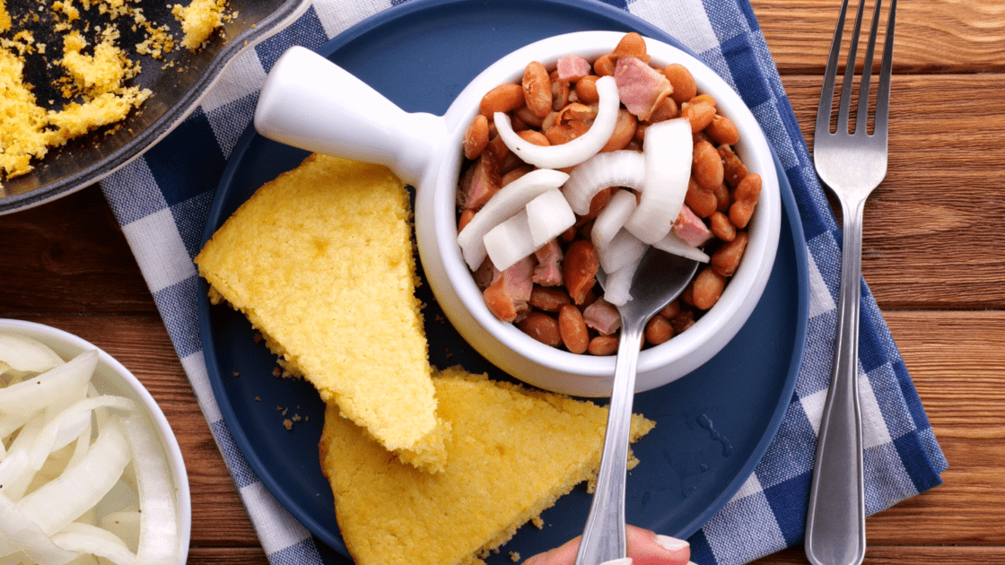 Bowl of pinto beans and ham with pickled onions on top and cornbread on side.
