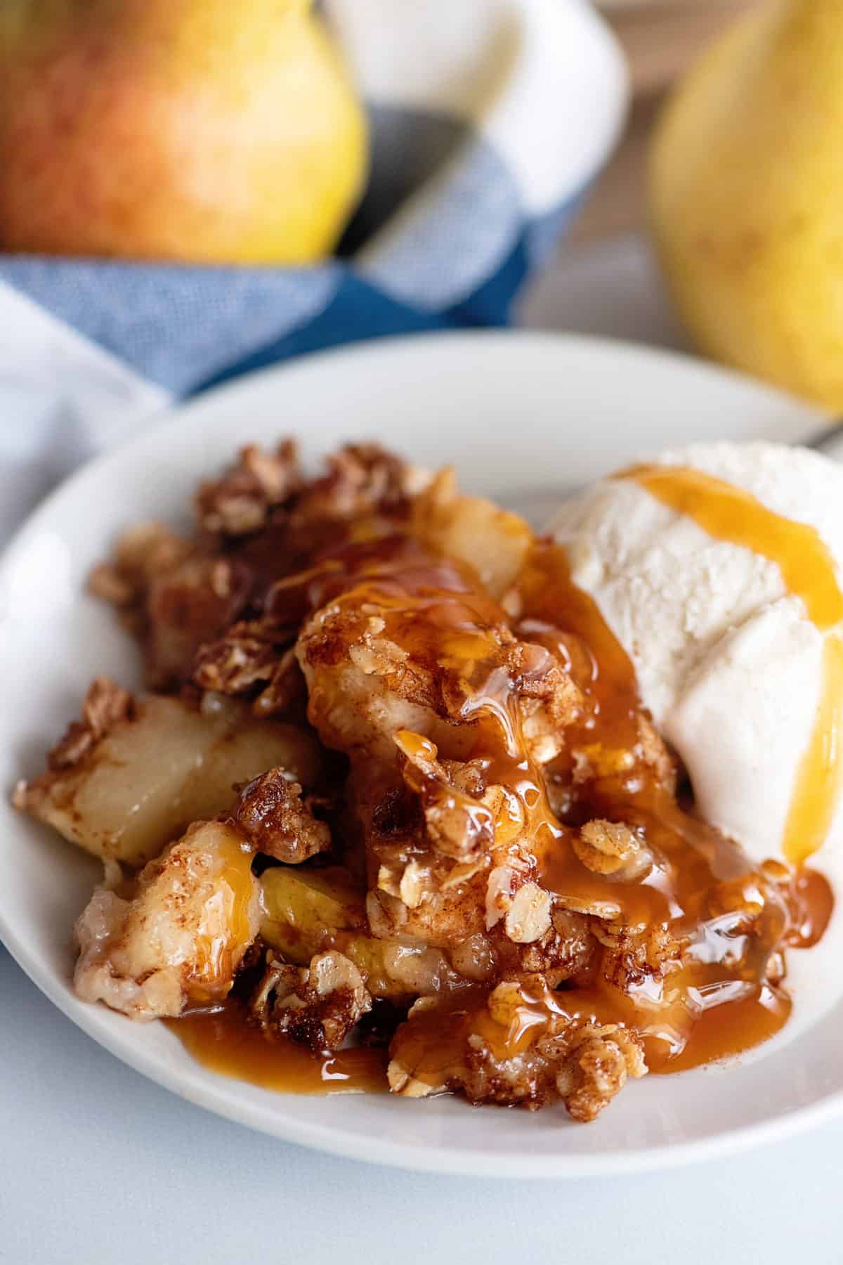 Pear crisp in bowl with scoop of vanilla ice cream.