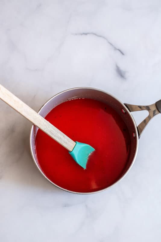 Red candy syrup mixture stirred together in a saucepan