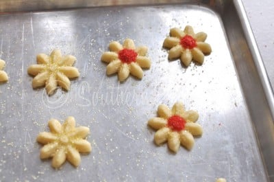 Adding red sprinkles to flower-shaped spritz cookies.