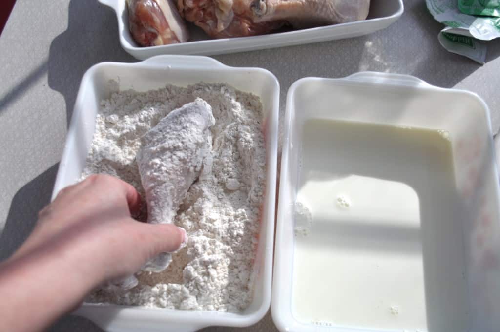 Fuss Free Fried Chicken - This is a way to actually fry chicken, in oil, in your oven A hand placing a flour coated chicken drumstick in a shallow dish of flour.