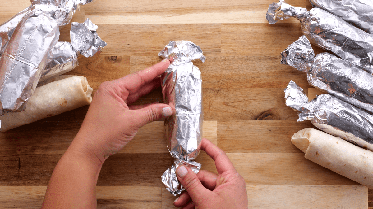 Rolled breakfast burritos in foil with twisted ends.