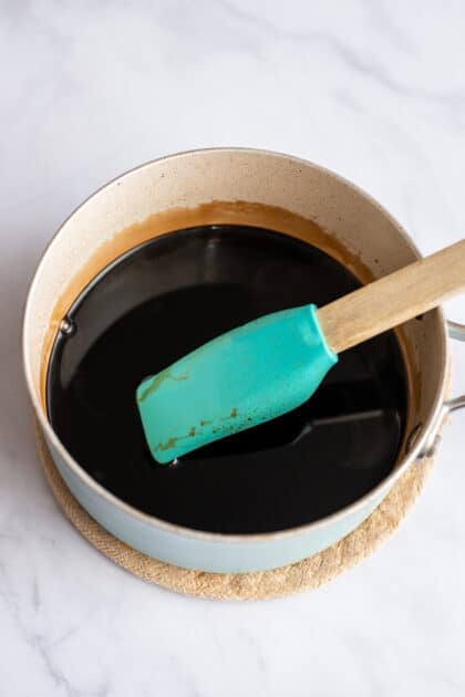 Stirring balsamic vinegar in a pot with a turquoise rubber spatula.