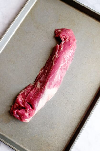 Raw pork tenderloin on a baking sheet.