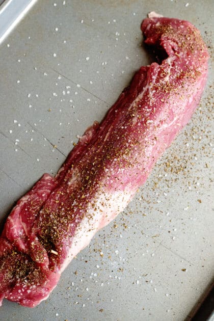 Seasoned, raw pork tenderloin on a baking sheet.