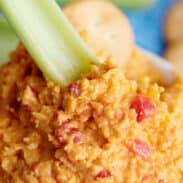 Celery stick dipping into spicy pimento cheese.